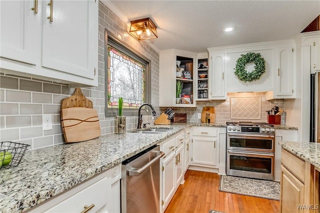 kitchen with a sink, white cabinets, light wood-style floors, appliances with stainless steel finishes, and decorative backsplash