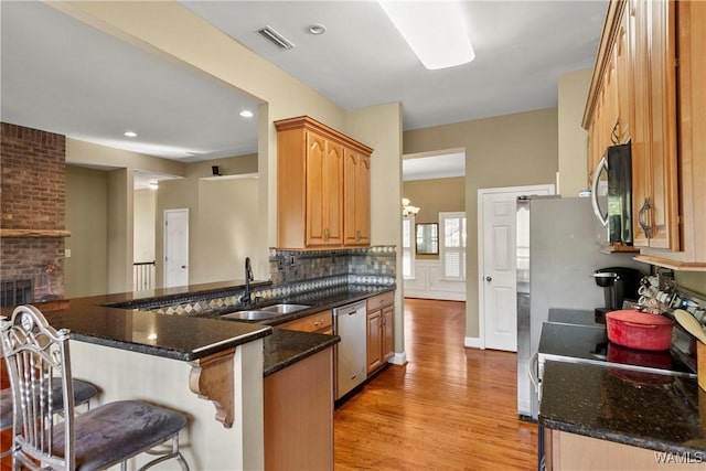 kitchen with a fireplace, dark stone countertops, kitchen peninsula, sink, and stainless steel appliances