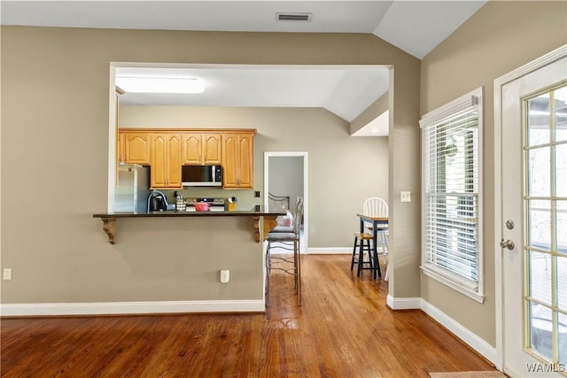 kitchen featuring vaulted ceiling, kitchen peninsula, a kitchen bar, wood-type flooring, and stainless steel appliances