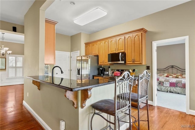 kitchen featuring kitchen peninsula, light hardwood / wood-style flooring, stainless steel appliances, and a notable chandelier