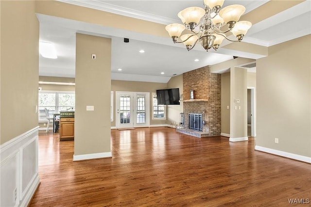 unfurnished living room with hardwood / wood-style floors, a brick fireplace, lofted ceiling, ornamental molding, and a chandelier