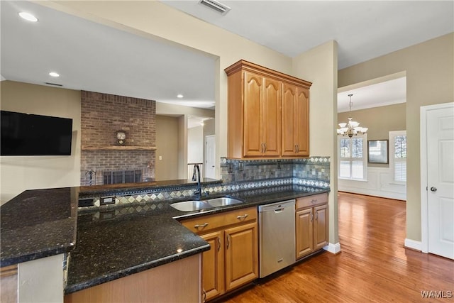 kitchen featuring dishwasher, dark stone counters, sink, kitchen peninsula, and hardwood / wood-style flooring