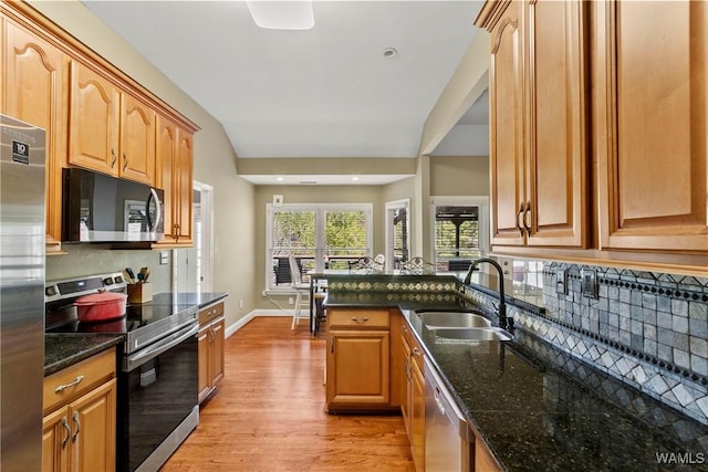 kitchen with appliances with stainless steel finishes, lofted ceiling, dark stone counters, and sink