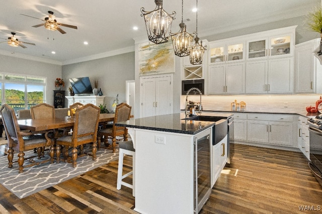 kitchen with dark hardwood / wood-style flooring, ornamental molding, a kitchen island with sink, and white cabinets