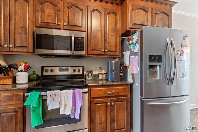 kitchen with brown cabinetry, appliances with stainless steel finishes, dark stone countertops, and crown molding