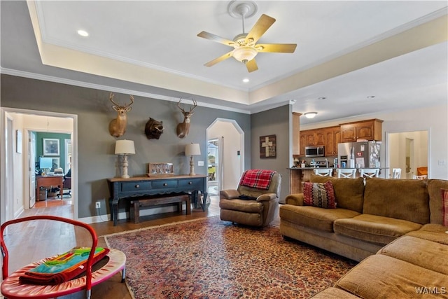 living room with arched walkways, a ceiling fan, a tray ceiling, and recessed lighting