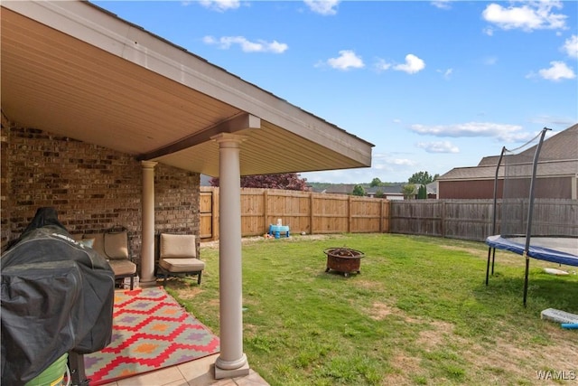 view of yard featuring a trampoline, a fenced backyard, and an outdoor fire pit