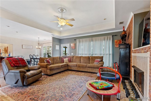living area featuring a fireplace, a tray ceiling, visible vents, and ceiling fan with notable chandelier
