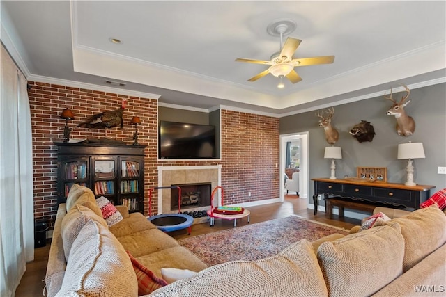 living area featuring ceiling fan, wood finished floors, a tray ceiling, and a fireplace