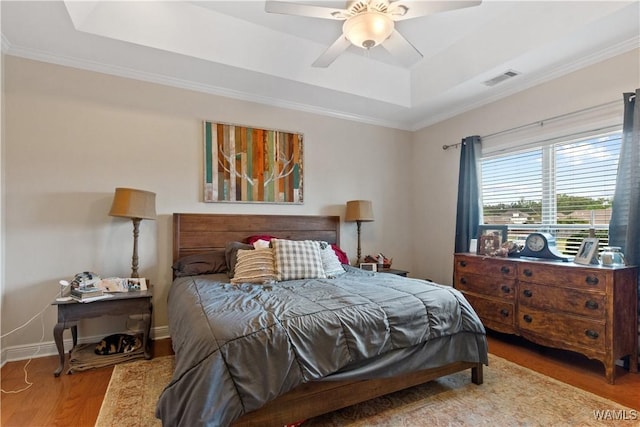 bedroom featuring ornamental molding, wood finished floors, a tray ceiling, and visible vents