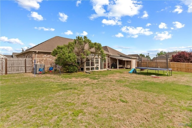 view of yard with a fenced backyard, a sunroom, and a trampoline