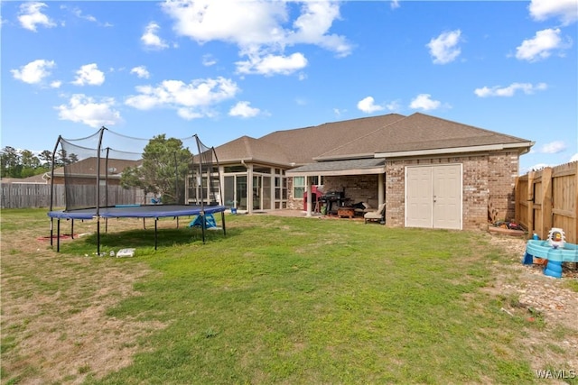 back of property featuring a trampoline, a fenced backyard, a yard, brick siding, and a sunroom