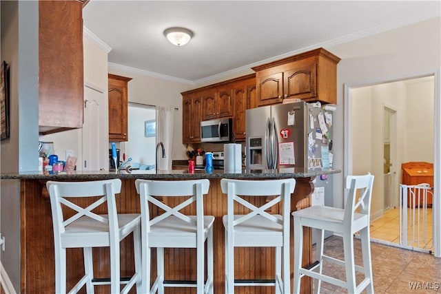 kitchen featuring dark stone counters, a breakfast bar, appliances with stainless steel finishes, a peninsula, and ornamental molding