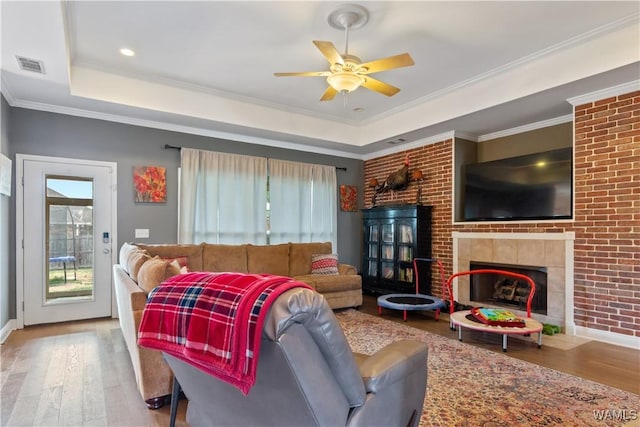 living area with visible vents, wood finished floors, ceiling fan, a fireplace, and a raised ceiling