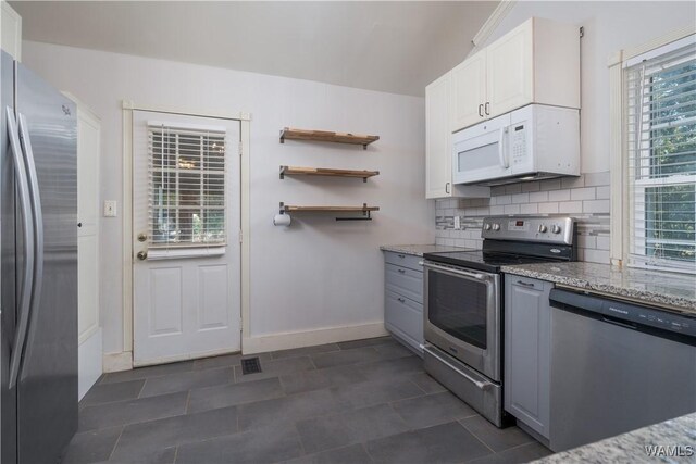 kitchen with stainless steel appliances, light stone countertops, white cabinets, and decorative backsplash