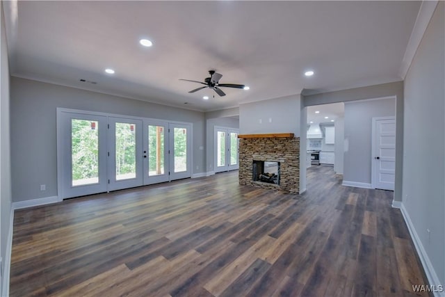 unfurnished living room featuring ceiling fan, a stone fireplace, ornamental molding, and dark wood-type flooring