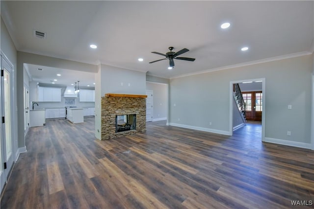 unfurnished living room featuring dark wood-type flooring, a stone fireplace, sink, ceiling fan, and ornamental molding