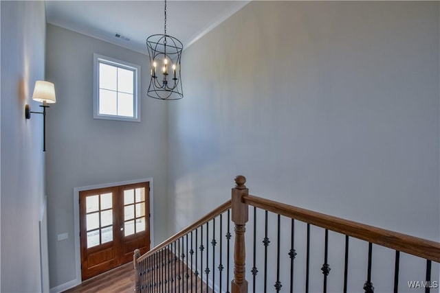 stairway with a chandelier, french doors, a healthy amount of sunlight, and wood-type flooring