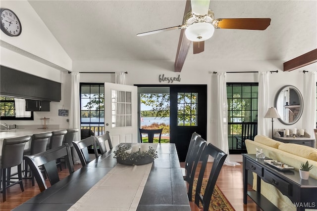 dining area featuring a textured ceiling, lofted ceiling with beams, a healthy amount of sunlight, and dark wood-type flooring