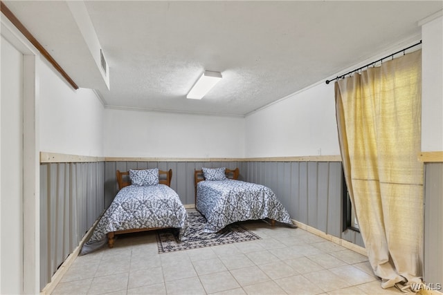 bedroom featuring wood walls, crown molding, light tile patterned floors, and a textured ceiling