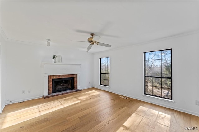 unfurnished living room with crown molding, ceiling fan, a brick fireplace, and light wood-type flooring