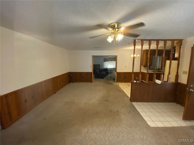 interior space with a wainscoted wall, a ceiling fan, a textured ceiling, carpet floors, and wooden walls