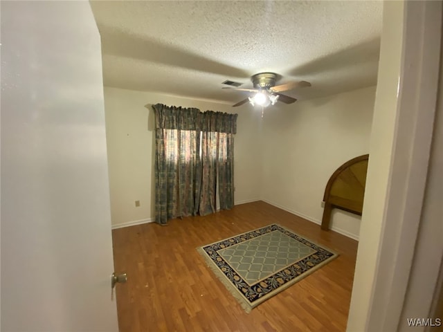 interior space with wood finished floors, baseboards, visible vents, ceiling fan, and a textured ceiling