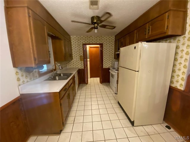 kitchen featuring wallpapered walls, white appliances, a textured ceiling, and a sink