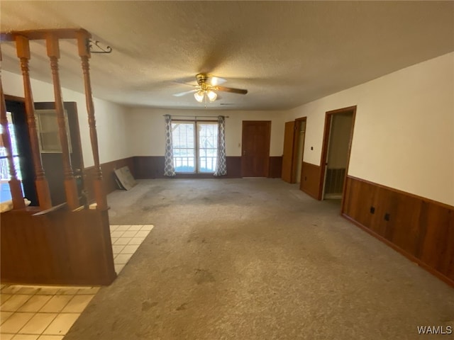 empty room with wooden walls, light carpet, wainscoting, a textured ceiling, and a ceiling fan