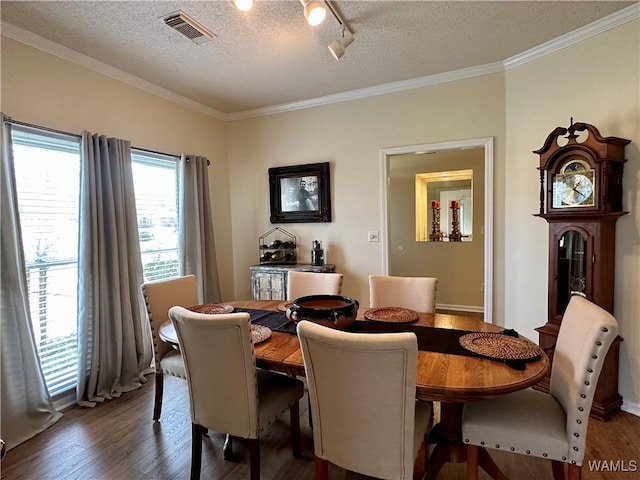 dining area with visible vents, dark wood-style floors, crown molding, a textured ceiling, and track lighting