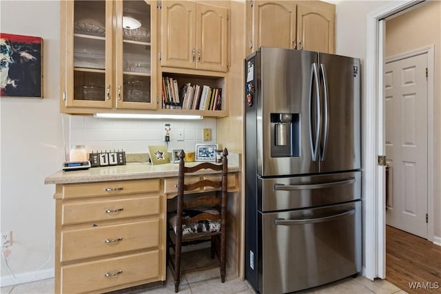 kitchen featuring stainless steel refrigerator with ice dispenser, light countertops, decorative backsplash, light brown cabinetry, and glass insert cabinets