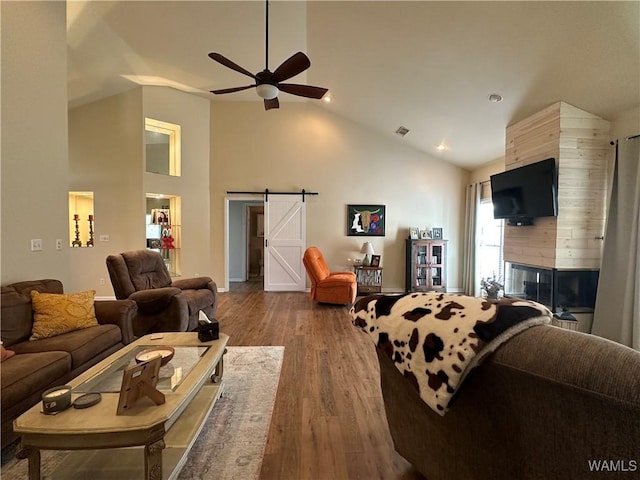 living area with a fireplace, a barn door, a ceiling fan, wood finished floors, and high vaulted ceiling