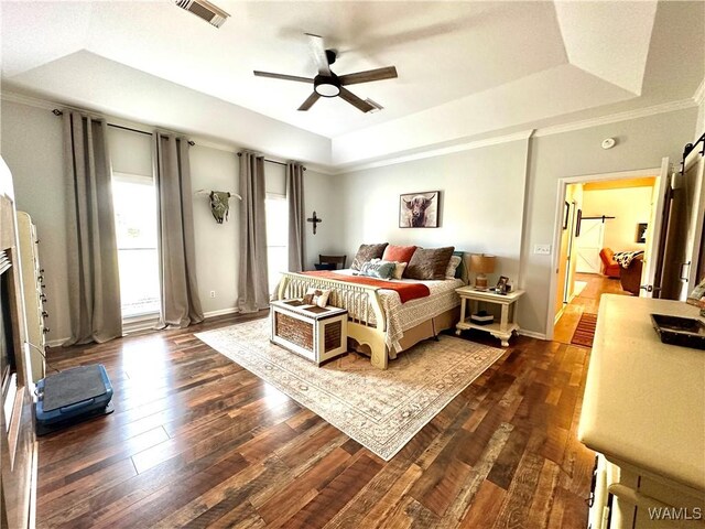 bedroom with a barn door, visible vents, dark wood finished floors, baseboards, and a tray ceiling