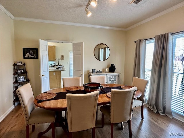 dining room with a textured ceiling, crown molding, wood finished floors, visible vents, and track lighting