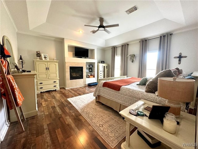 bedroom with a tray ceiling, dark wood-style flooring, a fireplace, and visible vents