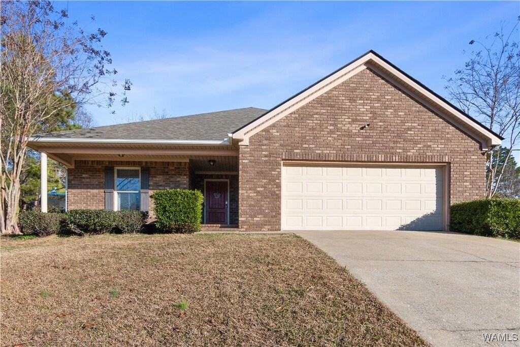 ranch-style home with driveway, brick siding, a front lawn, a shingled roof, and a garage