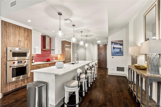 kitchen with wall chimney exhaust hood, sink, a center island with sink, electric stovetop, and pendant lighting