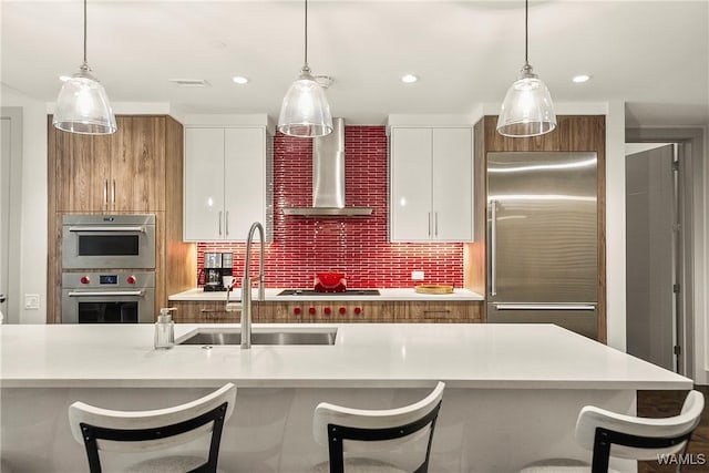 kitchen featuring pendant lighting, white cabinetry, sink, stainless steel appliances, and wall chimney range hood