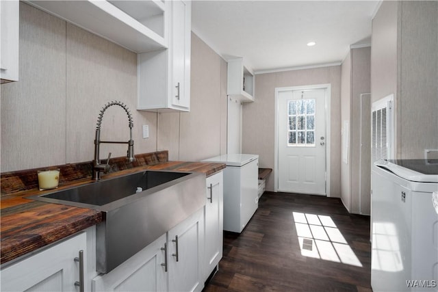 kitchen featuring dark wood-type flooring, a sink, washer / clothes dryer, white cabinetry, and wooden counters