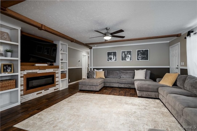 living area with built in shelves, a ceiling fan, dark wood-type flooring, a textured ceiling, and a glass covered fireplace