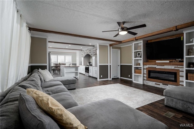 living area with a glass covered fireplace, dark wood-type flooring, ceiling fan, and a textured ceiling