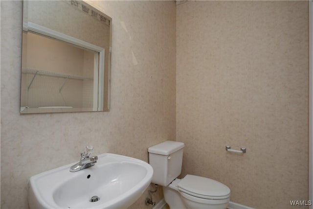 bathroom with wallpapered walls, toilet, and a sink