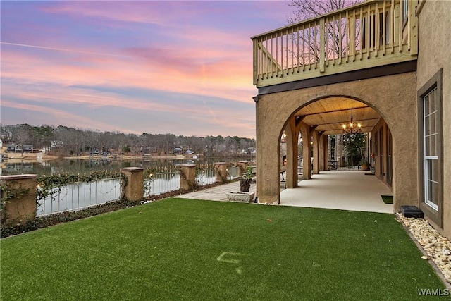 yard at dusk with a water view, fence, and a patio