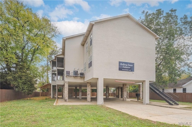 back of house featuring a yard, concrete driveway, stairway, fence, and a carport