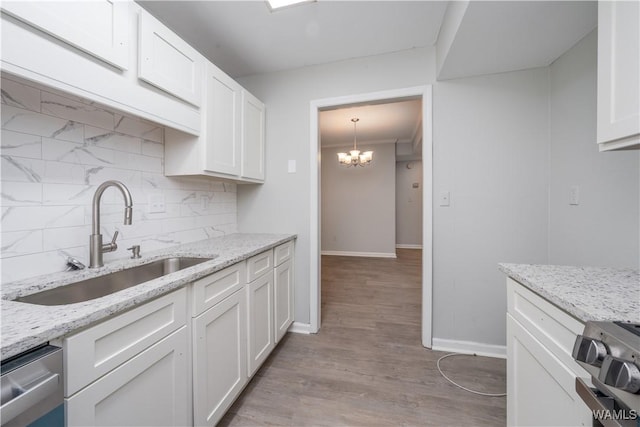 kitchen featuring stainless steel appliances, backsplash, an inviting chandelier, white cabinets, and a sink