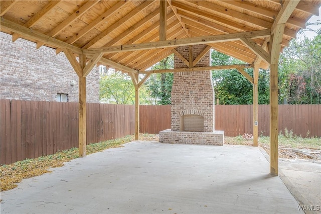 view of patio featuring an outdoor brick fireplace, a fenced backyard, and a gazebo