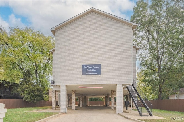 view of front of home featuring brick siding, stairway, fence, a carport, and driveway