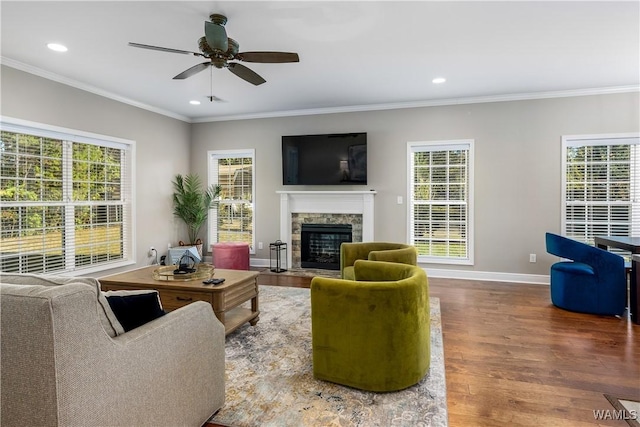 living area with wood finished floors, crown molding, plenty of natural light, and a fireplace