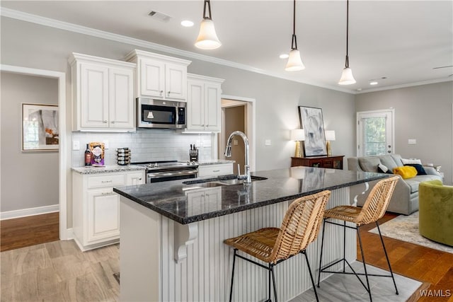 kitchen with a sink, open floor plan, appliances with stainless steel finishes, light wood finished floors, and decorative backsplash