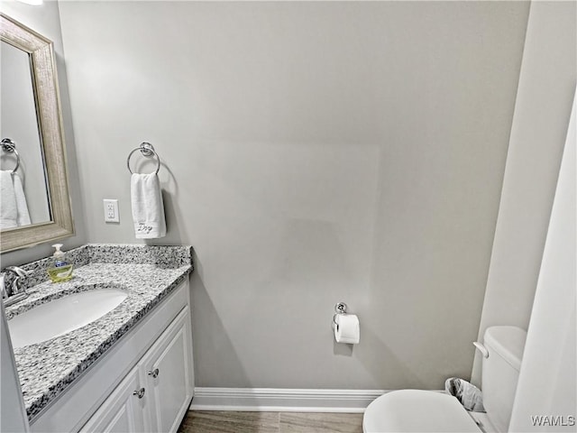 bathroom featuring toilet, vanity, baseboards, and wood finished floors